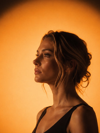 Elegant female side profile portrait under warm circular spotlight, minimalist moody aesthetic homepage hero image for Duska brand, premium lifestyle visual design.