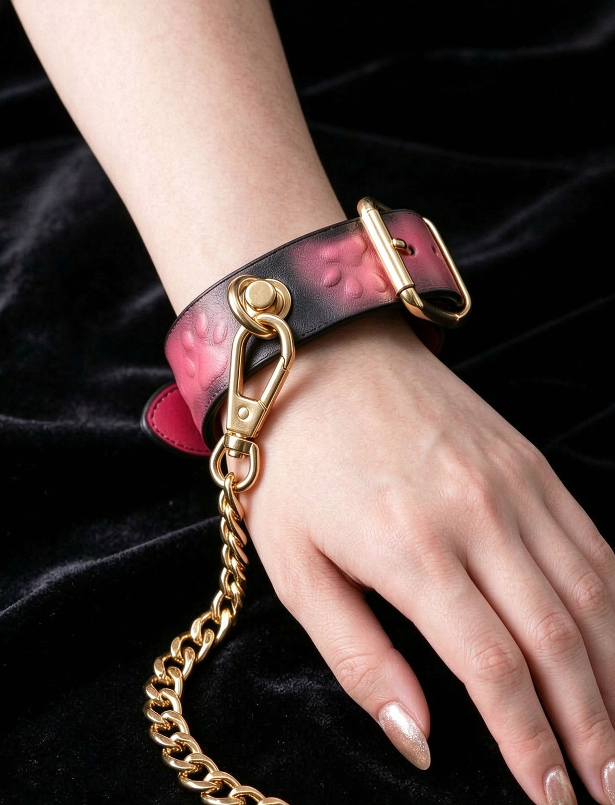 handchain thermochromic leather wrist cuff with embossed paw print pattern heat reactive pink marks polished gold metal buckle and chain worn on wrist black velvet background