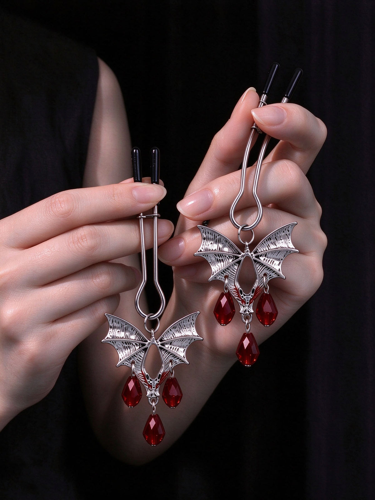 close up of silver bat wing jewelry for nipple with red teardrop crystal pendants on soft black velvet fabric gothic accessory couples gifts