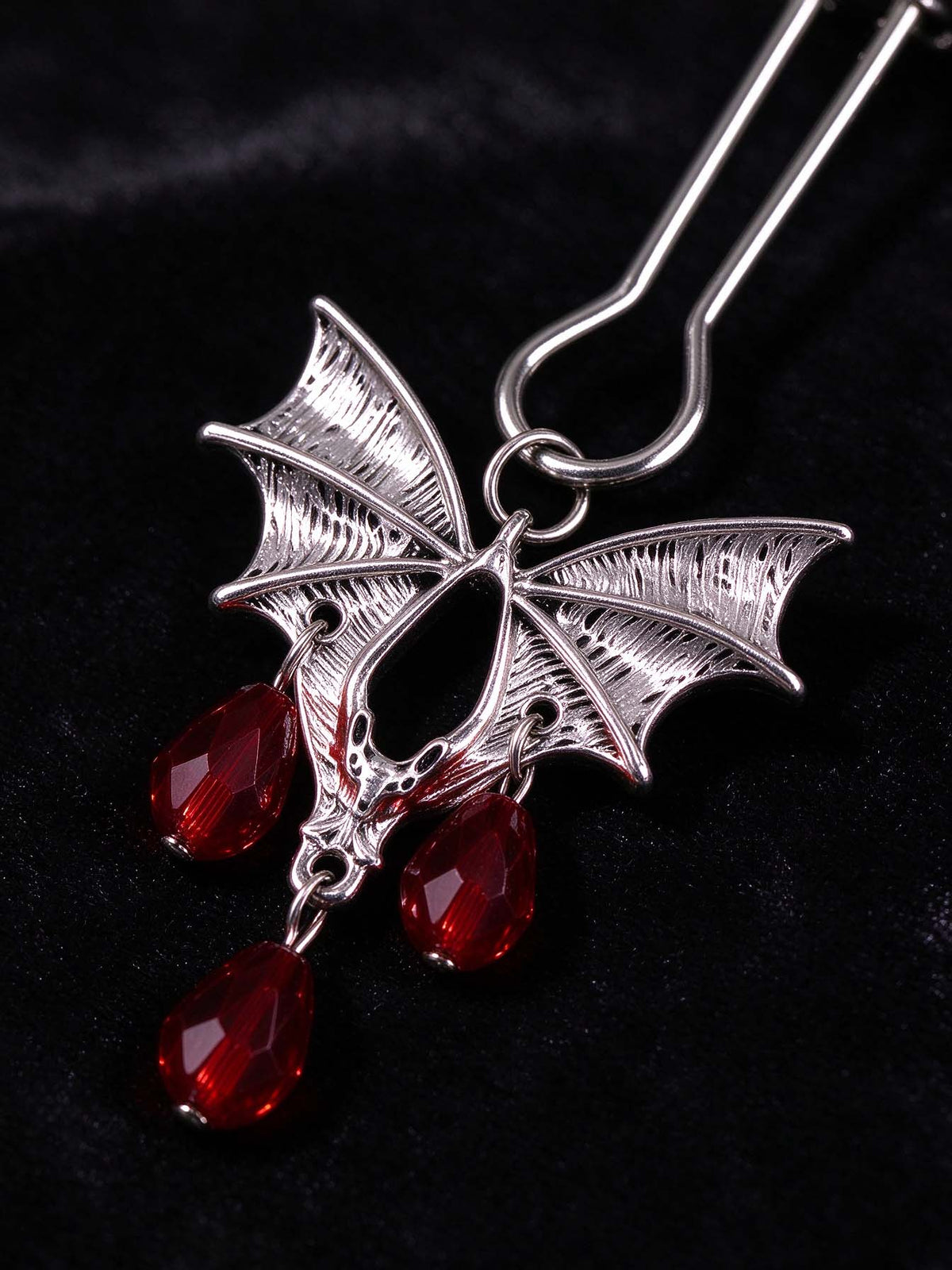 close up of gothic bat charm for nipple clamps antique silver bat pendant with teardrop red crystal beads dark velvet surface goth fashion decorative jewelry