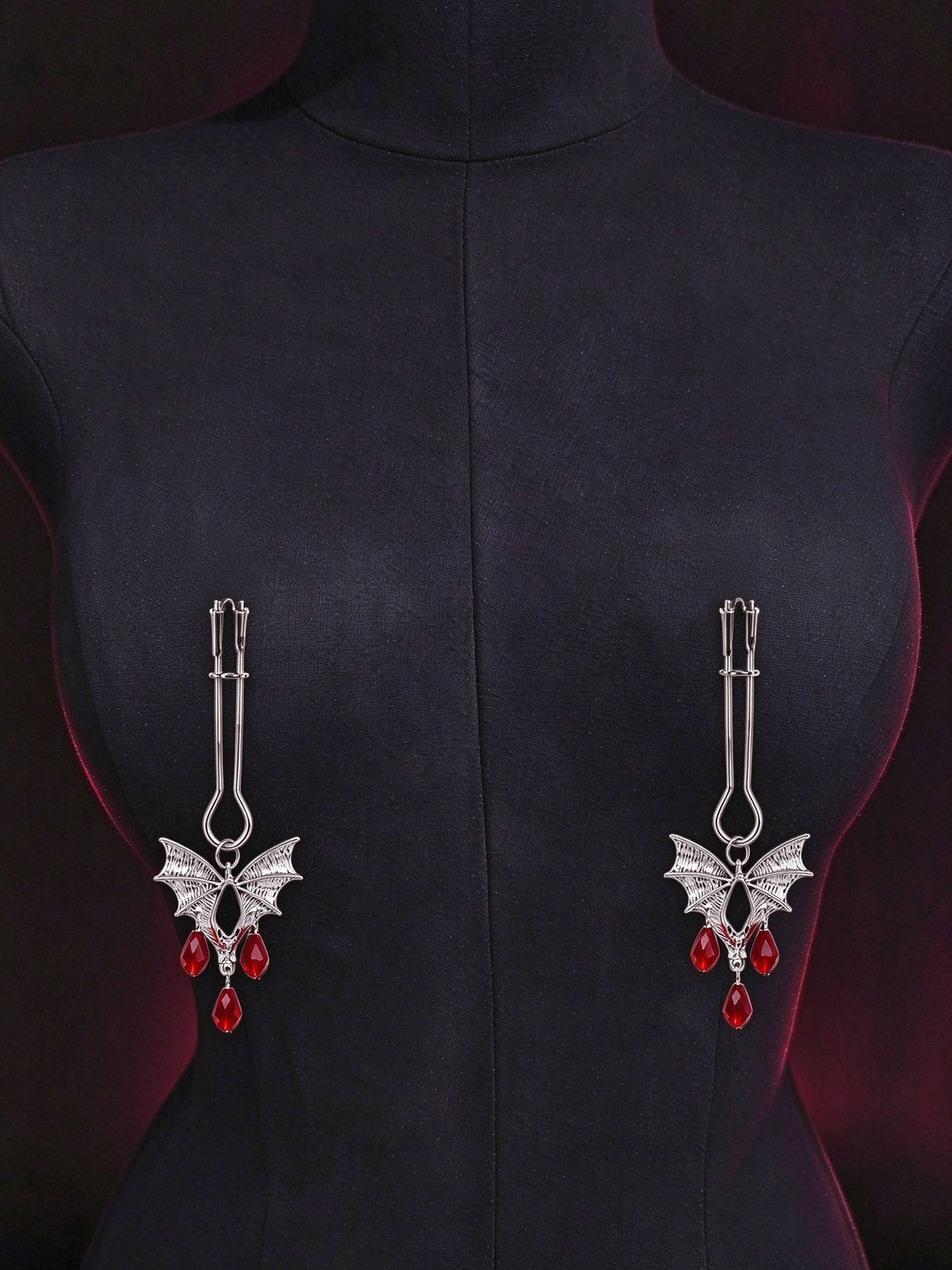 gothic bat nipple clamps antique silver bat charm with teardrop red crystal pendants displayed on black fabric mannequin dark red mood background goth decorative fashion jewelry