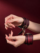 Pair of thermochromic leather handcuffs worn on both wrists, dark brown leather with red pink heat reactive gradient, gold D rings and chain, deep red studio background