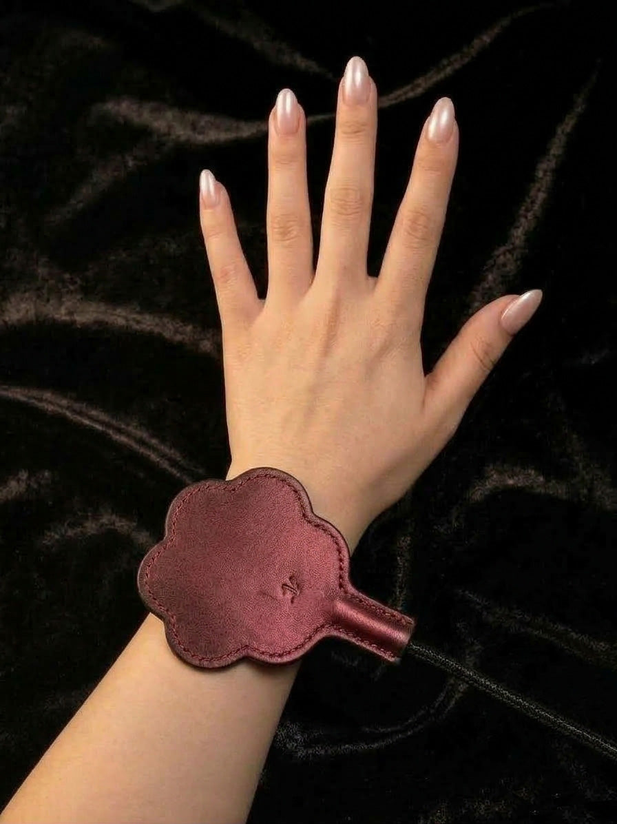 Back side of thermochromic leather paw paddle strapped on wrist, plain dark red gradient leather pad with red stitching, worn detail shot