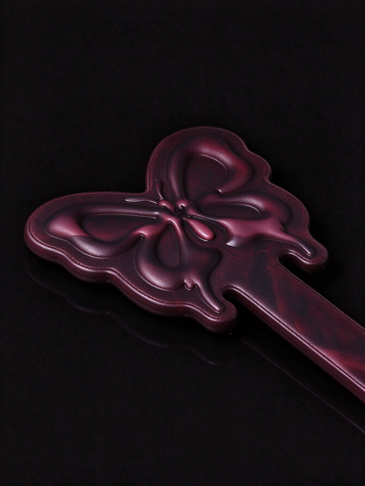 close up shot of thermochromic leather butterfly paddle embossed butterfly head deep plum leather on black reflective surface