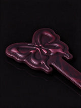 close up shot of thermochromic leather butterfly paddle embossed butterfly head deep plum leather on black reflective surface