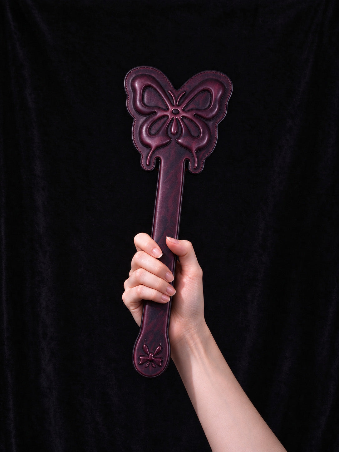 hand holding thermochromic leather butterfly paddle embossed butterfly pattern dark purple leather accessory black velvet background