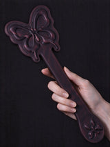 hand holding thermochromic leather butterfly paddle full product view embossed butterfly pattern dark plum leather dark fabric background