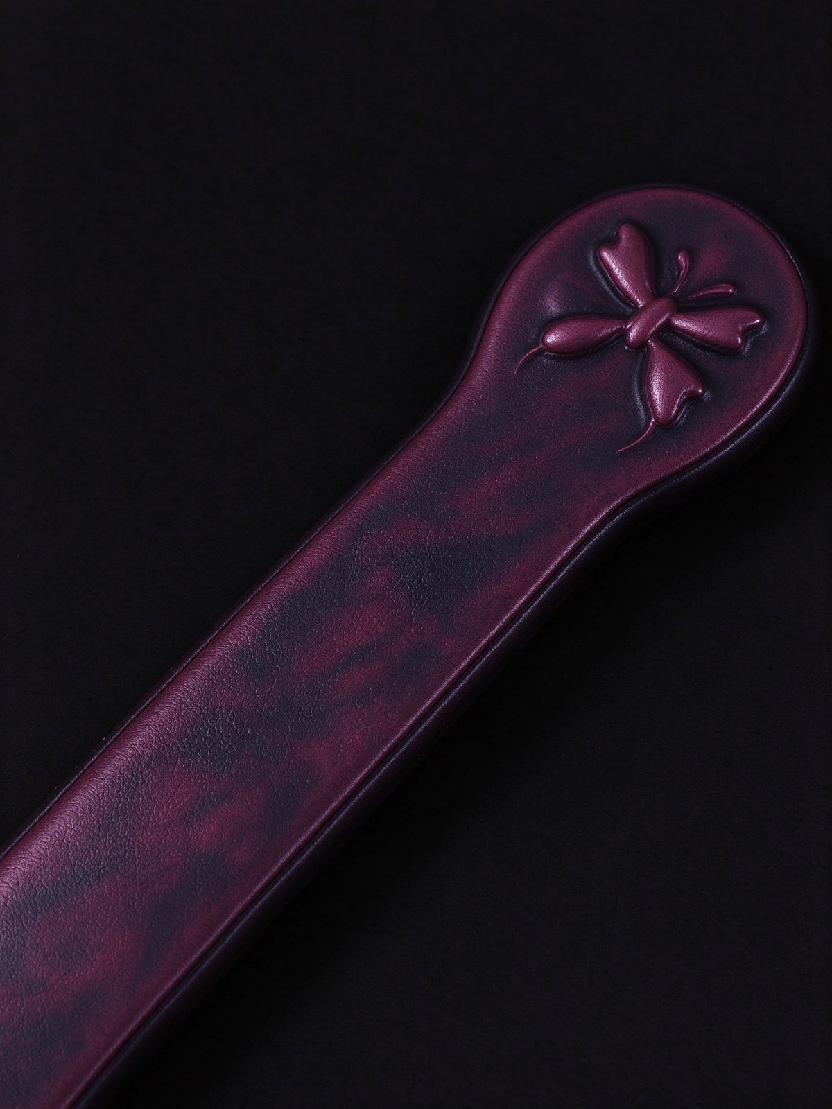 close up of thermochromic leather butterfly paddle handle tail embossed small butterfly pattern deep plum leather dark background