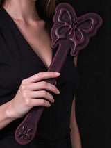 model holding thermochromic leather butterfly paddle embossed butterfly design deep plum leather dark background lifestyle shot