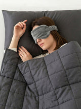 Woman resting under a weighted blanket for adults, wearing a sleep mask